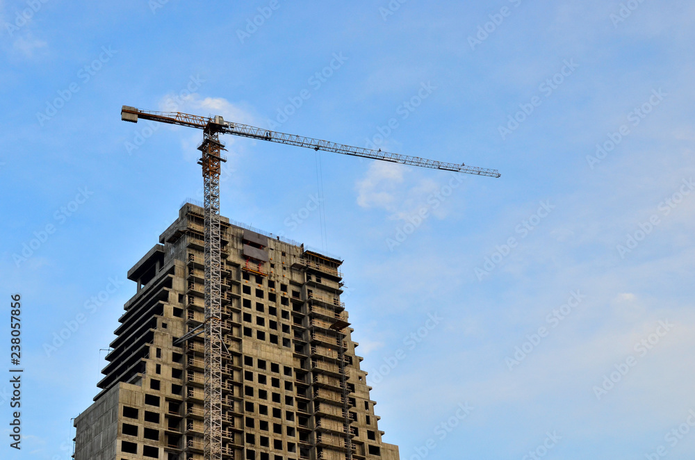 Fototapeta premium Crane and building construction site against blue sky with blank white billboard for advertisement at the top of tower architecture on the background of the sky