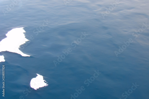 two snow islets on thick dark-blue ice; frozen ripples on water surface, close-up