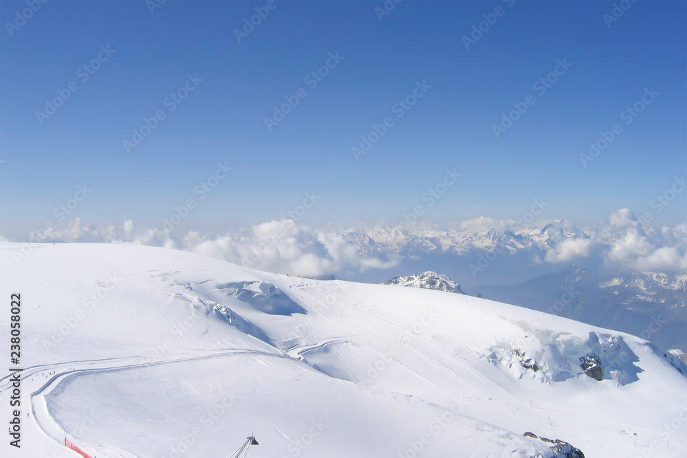 long alpine skiing track from the very top of mount; low clouds over a mountain range and a deep gorge hidden in blue haze; Swiss Alps