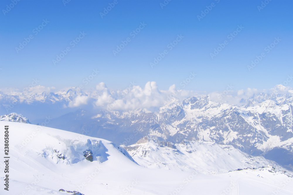 inspiring top view of a vast mountain range and accumulating cumulus clouds between snowy peaks; a gentle slope running down from the very top of glacier, Switzerland