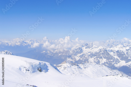 inspiring top view of a vast mountain range and accumulating cumulus clouds between snowy peaks  a gentle slope running down from the very top of glacier, Switzerland © Elena