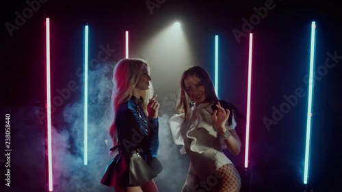 Two sexy women dancing gogo in a club with neon light. Blonde and brunette young girls clubbing together. Shoot with RED RAVEN camera. 