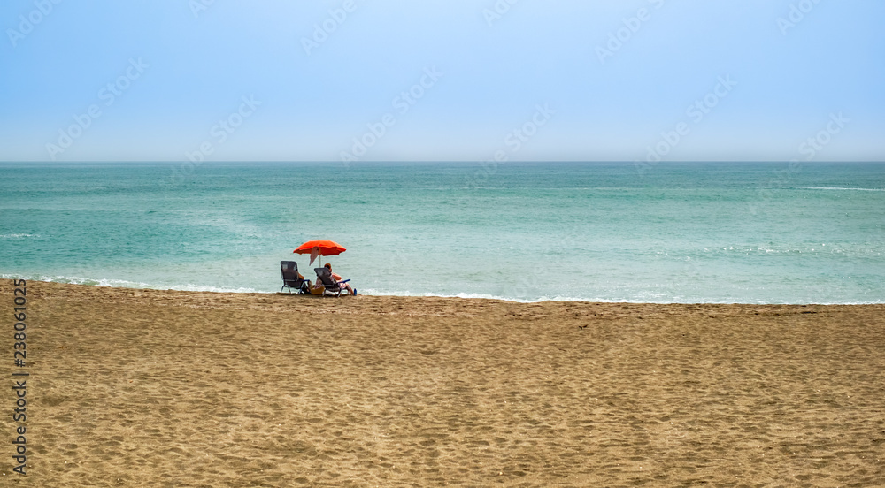 Beach summer couple on vacation holiday relax in the sun on their deck chairs under a red umbrella