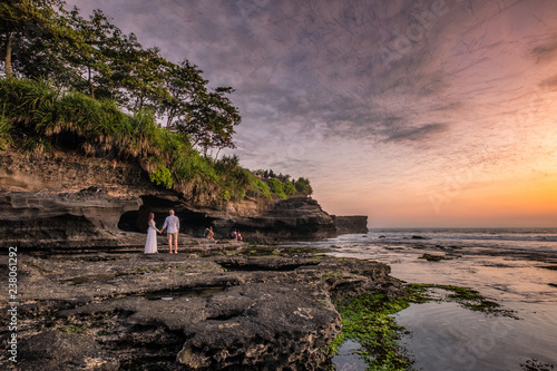 Lovers are watching flock of bats from cave on coastline at sunset