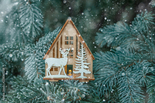 Christmas Toy house is wrapped in a warm scarf  it s snowing.on a natural natural background of a real fir in the snow  toned. Concept of winter  Christmas  new year  warm  cozy  loving  protecting .