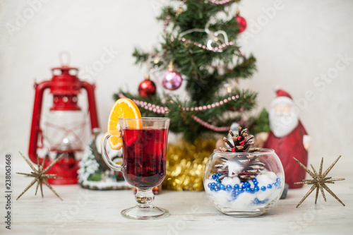 Christmas decor, tree, gold pumpkin, bump in glass vase, red lantern on the wooden table. White wood background Hot mulled wine drink with orange in a glass cup Christmas eve