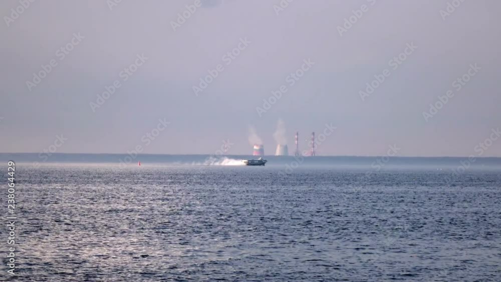 View from the coast on the high-speed Raketa (hydrofoil) ship going across the Gulf of Finland against the background of thermal power plant in summer sunny day View from the coast on the high-speed Raketa (hydrofoil) ship going across the Gulf of Finland against the background of thermal power plant in summer sunny day
