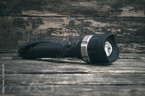 Black flashlight on the wooden table background.