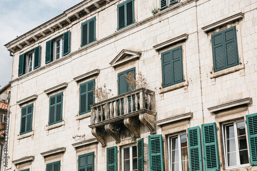 Naklejka premium The facade of an ordinary old building with windows and a balcony in Montenegro. Some windows are closed by shutters. Traditional housing.