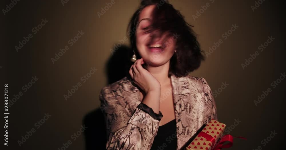 Brunette happy woman hold her present, spin with confetti in pink background wear red dress Brunette happy woman hold her present, spin with confetti in pink background wear red dress