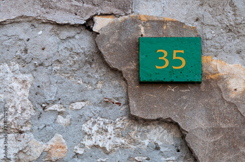 Green square sign with building number 35 in yellow on a partly damaged wall background photo