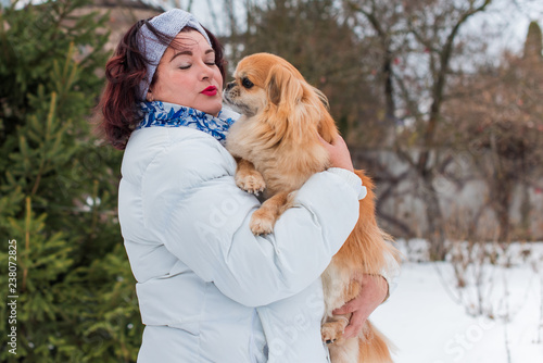 Christmas, winter holidays concept. Beautiful plus size woman with red pekingese dog at park. Love and care for pets