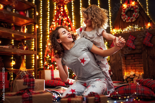 Cheerful cute curly little girl and her older sister exchanging gifts. Sisters having fun near christmas tree indoors. Loving family with presents in christmas room.