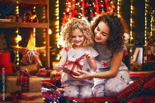 Cheerful cute curly little girl and her older sister exchanging gifts. Sisters having fun near christmas tree indoors. Loving family with presents in christmas room. © zamuruev