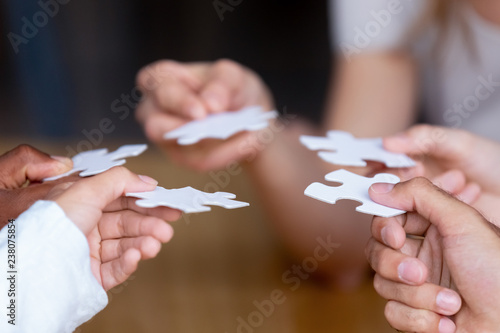 Diverse multinational businesspeople or best friends holding white pieces of puzzle jigsaw  close up female and male hands. Teamwork and friendship symbol strategy and solving problem together concept