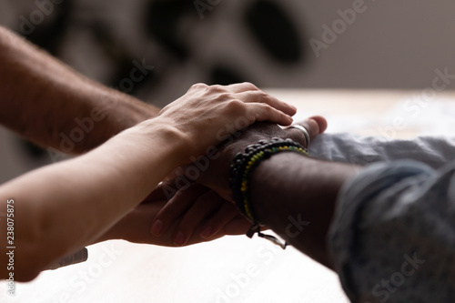 Close up diverse male female sitting holding hands together. Multiracial people starting common business or celebrate success at work stacked hands together showing unity support, all for one concept