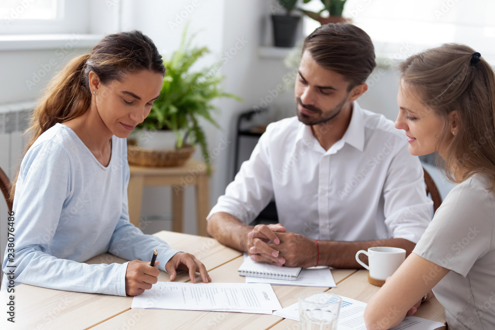Fototapeta premium Mixed race client hold pen put signature at official paper make buy or sell deal sitting with partners during meeting. After successful job interview millennial woman signing employment agreement