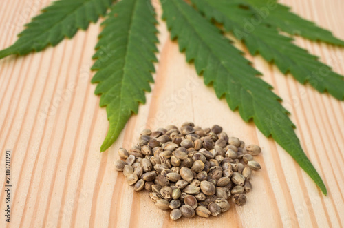 Hemp seeds and a blurred cannabis leaf against a background of wood texture.