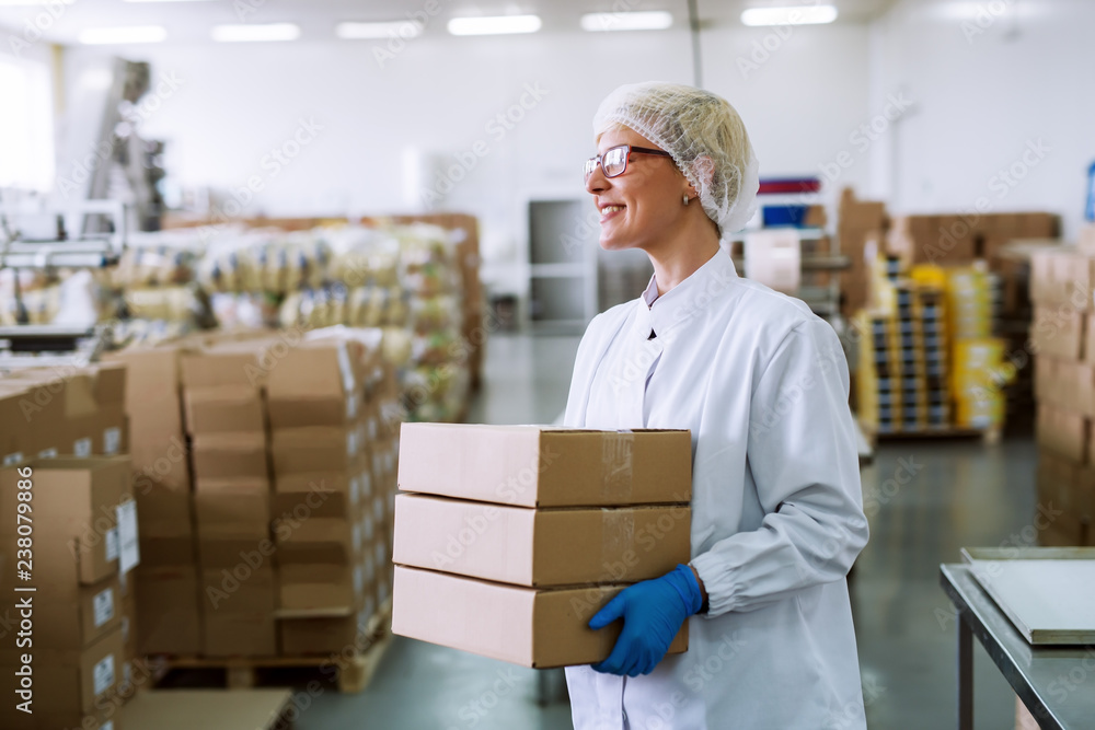 Happy Caucasian female worker holding boxes while standing in warehouse. Happy Caucasian female worker holding boxes while standing in warehouse.
