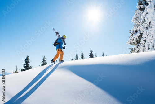 Картината върху платно Low angle shot of a skier walking on top of the mountain with his skis on his shoulder on a sunny winter day sunlight nature recreation skiing lifestyle downhill sportive concept
