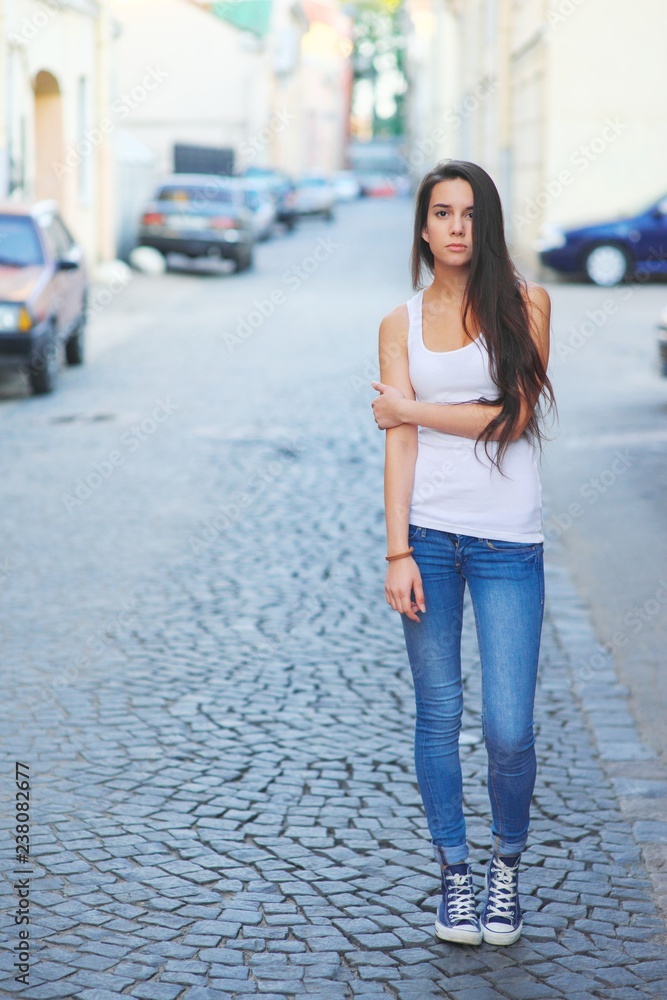 Hipster girl wearing blank white t-shirt and jeans posing against street road, minimalist urban clothing style, mockup for tshirt print store