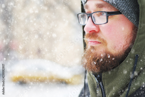 Portrait of a young bearded man frozen in a Blizzard in the woods. Face, beard , mustache and glasses covered with frost.