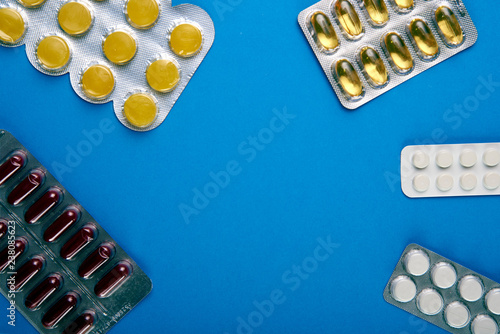 Many different types of drugs lie in a circle. Burgundy capsules, yellow lollipops from sore throat, fish oil pills, simple white tablets. In center of circle is a place for your text, advertising.