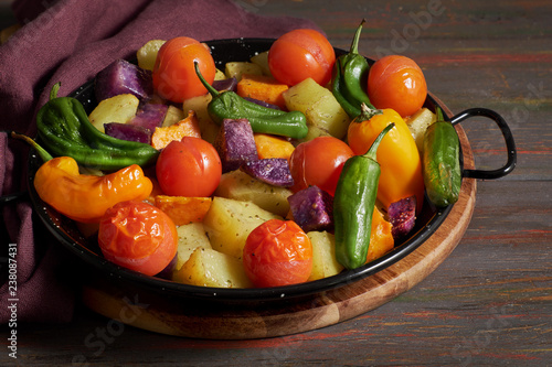 Rustic, oven baked vegetables in baking dish. Seasonal vegetarian vegan meal on dark wooden background with linen towel.