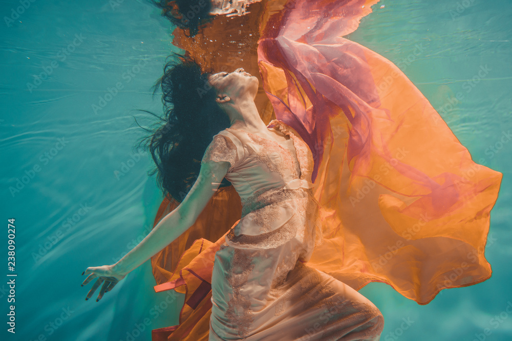 Φωτογραφία girl with orange dress is dreamy and meditative floating under water, like the s
