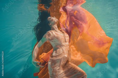 girl with orange dress is dreamy and meditative floating under water, like the soul before reincarnation photo