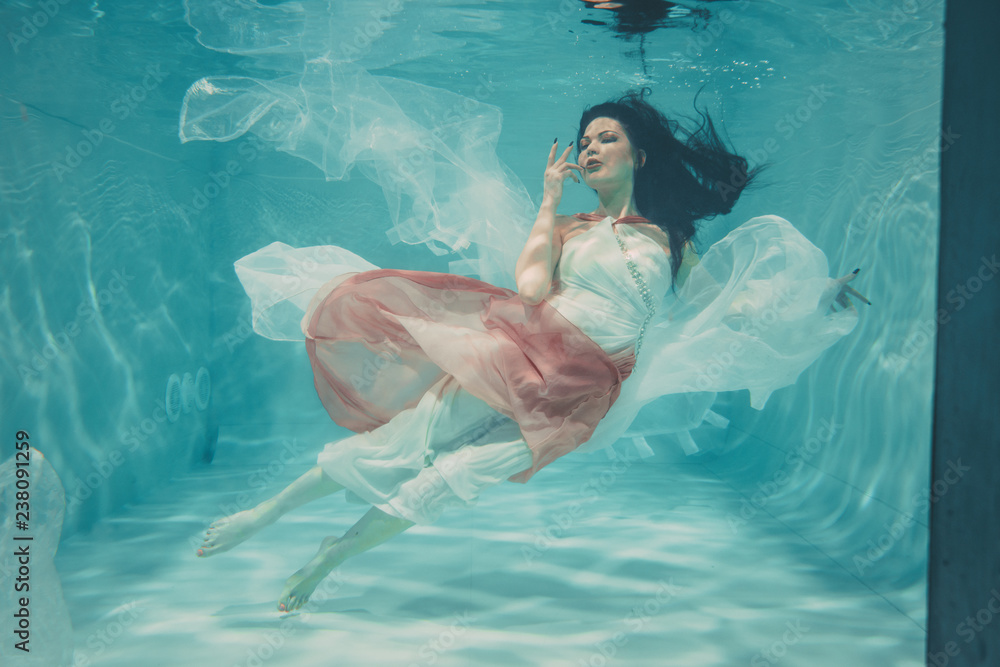 beautiful model girl swimming underwater in feminine long white and pink dress Stock Photo