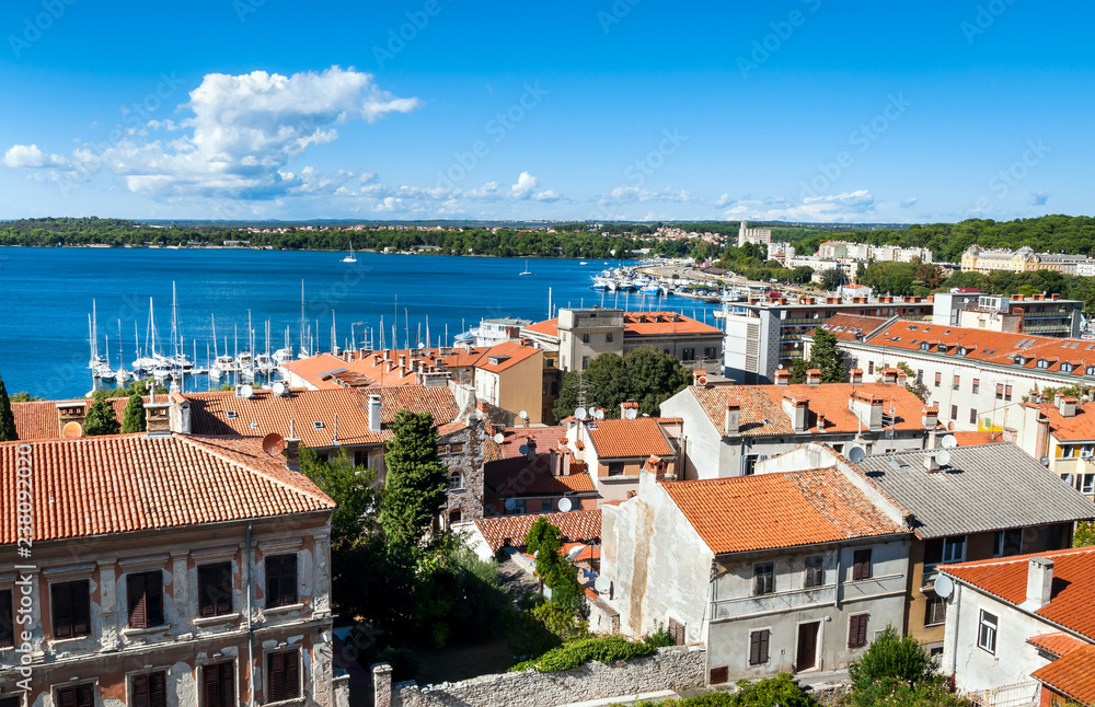 Panoramic view of Pula with orange tile buildings roofs and blue harbor, Istria region, Croatia