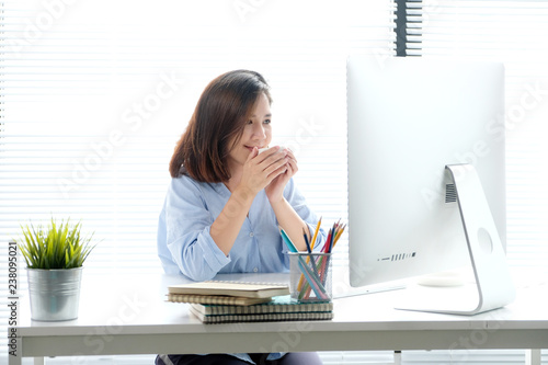 Young asian woman holding a coffee cup with smiling face while working with computer, positive emotion at working desk background, casual office life, working at home concept