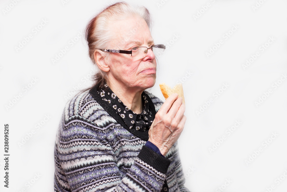 old, elderly woman, eating bread is frustrated with life. White background. Close up old, elderly woman, eating bread is frustrated with life. White background. Close up