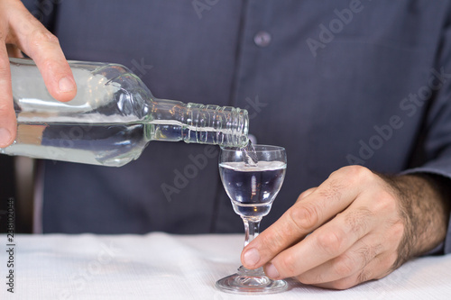 Męska dłoń nalewa wódkę z butelki do kieliszka.