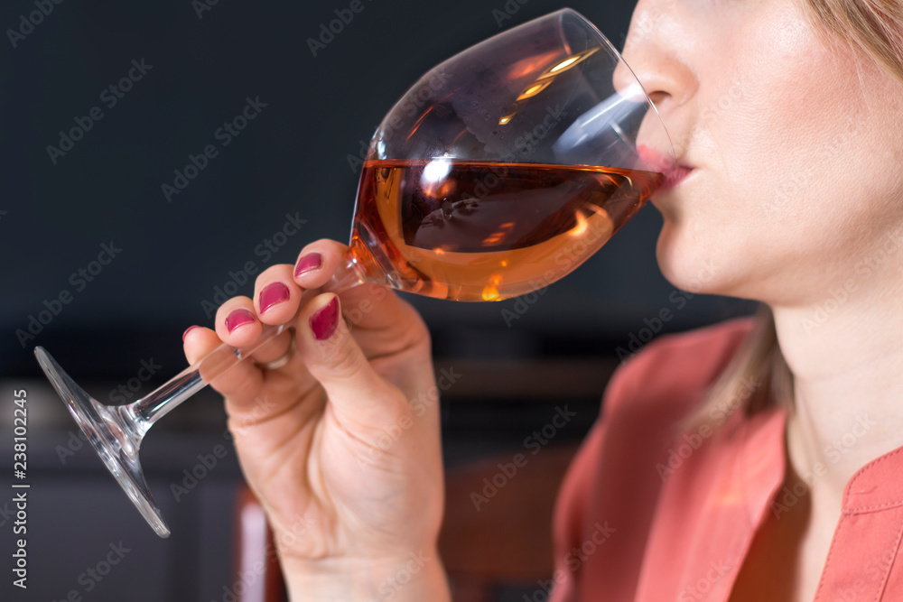 Biała młoda kobieta trzyma kieliszek do wina przystawiony do ust i pije z niego wino. - obrazy, fototapety, plakaty 