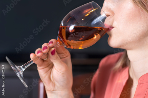 Biała młoda kobieta trzyma kieliszek do wina przystawiony do ust i pije z niego wino.