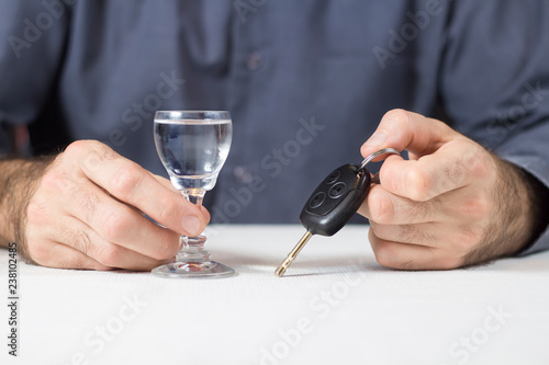 Męska dłoń trzyma kieliszek z wódką. W drugiej ręce kluczyki od samochodu.
