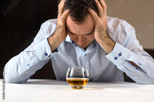 Na kłopoty alkohol. Załamany mężczyzna siedzi przy stole z głową w dłoniach. Szklanka whisky stoi przed nim.