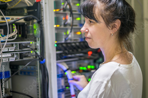 The girl works in the server room of the data center. Portrait of a woman against a background of powerful computer equipment.