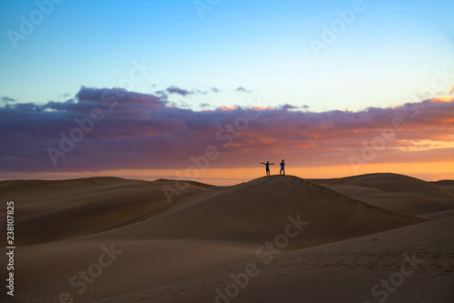 Silhouette of two men taking picture of dusk scenery at famous dunes in Maspalomas, Gran Canaria, Spain