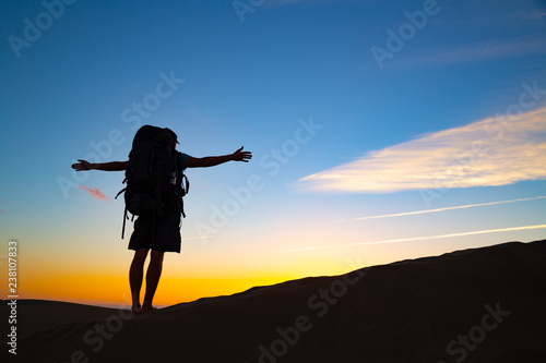 Silhouette of hiker man with hiking bag on top dunes in Maspalomas, Gran Canaria, Spain