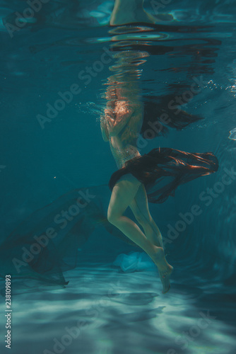 beautiful girl in a transparent jumpsuit with rhinestones on the whole body swims underwater as a free diver