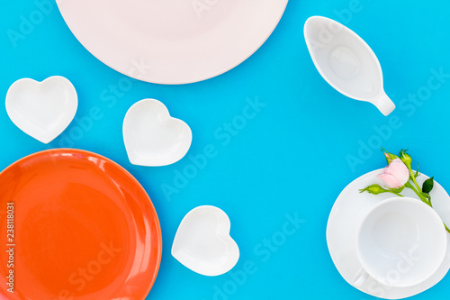 Simple color table setting for celebration with roses, orange plates and heart-shaped saucers on blue table background top view mock up