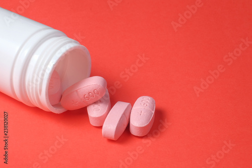 White pills and bottle on red background