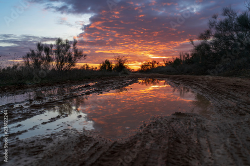 Puddle on a path in the field in which the sunset is reflected, with orange, yellow and blue colors.