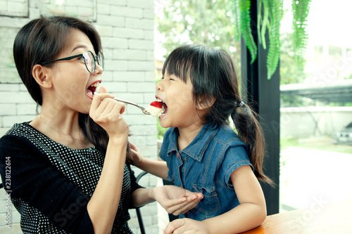 asian woman and daughter eating strawberry cake in home living room