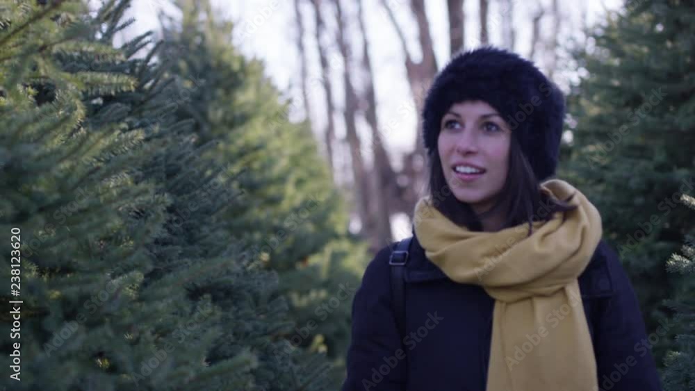Beautiful woman in winter walks through rows of christmas trees looking for the perfect tree - close up on face Beautiful woman in winter walks through rows of christmas trees looking for the perfect tree - close up on face