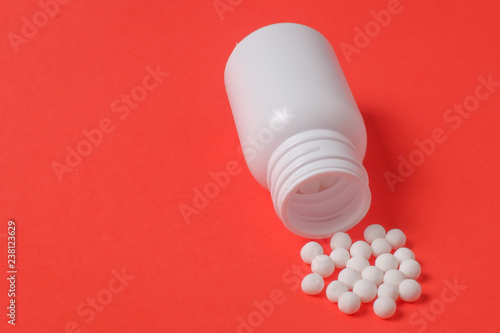 White pills and bottle on red background