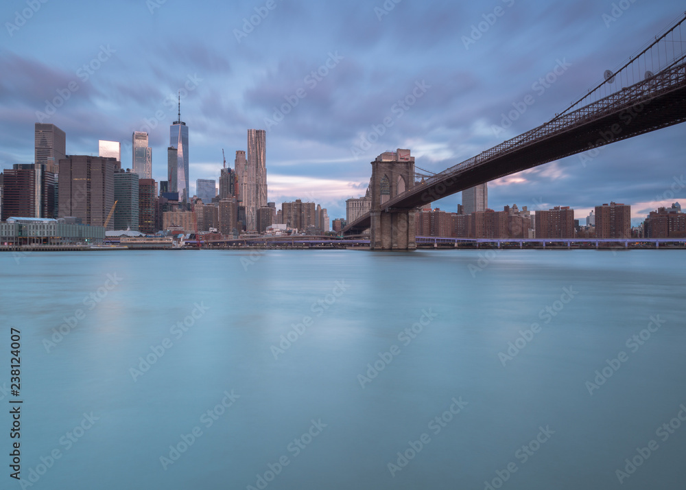 View on Brooklyn Bridge and financial district from east river at sunrise with long exposure